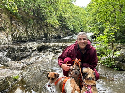 Jess, out for a walk with her three terriers beside some river rapids.