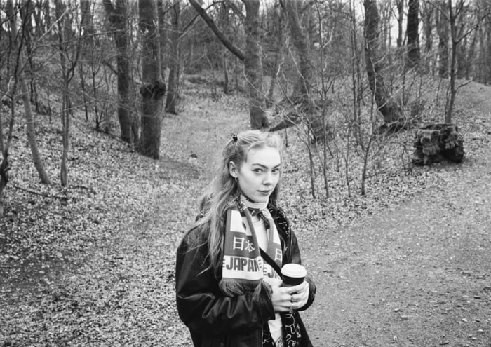 A young woman poses in a forest clearing in this black and white photograph.
