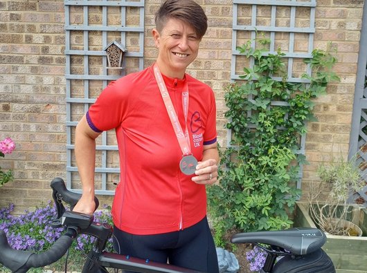 A female cyclist smiles holding their medal in front of their bike having completed the Ride London event