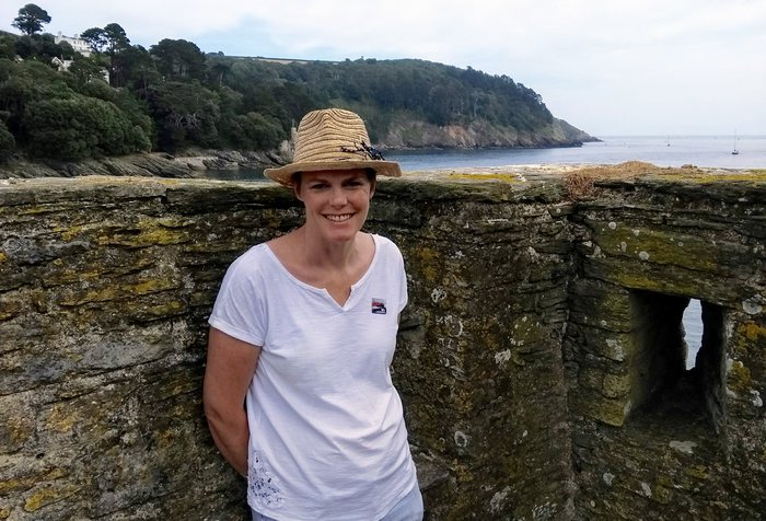 Joanna, who is living with blood cancer, wearing a sun hat in a ruin, overlooking a headland and the sea.