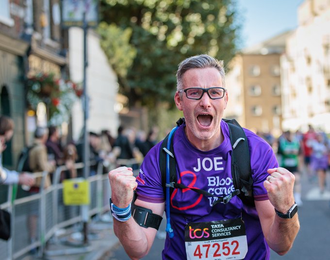 Male Blood Cancer UK runner looking directly into the camera and celebrating with both fists in the air