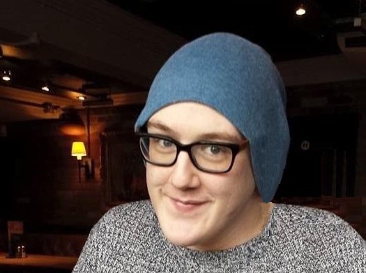 Josh sitting in a bar smiling, wearing a hat and a jumper.