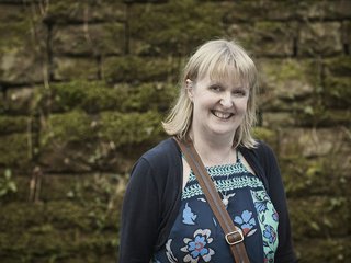 An image of Kate, who was diagnosed with non-Hodgkin's lymphoma, smiling and standing to the left of a wall.