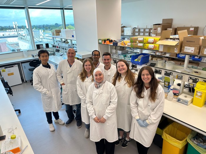 Dr Batta and his lab team stood in the lab wearing their lab coats smiling at the camera