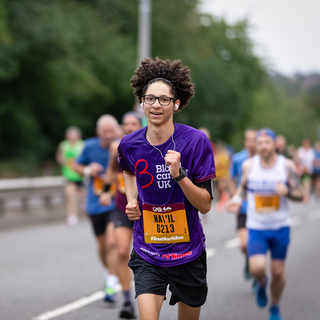 A male running on a road wearing a purple blood cancer UK t shirt during a marathon.