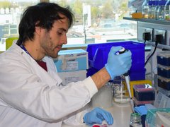 A man with dark hair wearing a white lab coat sat working in the lab.
