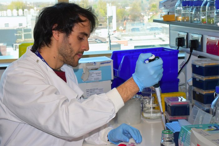 A man with dark hair wearing a white lab coat sat working in the lab.