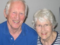 A close up image taken at home of an old couple smiling.