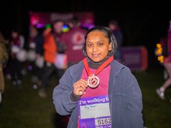 A participant showing off their gold medal under the night sky at the Walk of Light event.