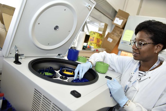 A researcher, wearing a white lab coat, in a lab loading a centrifuge.