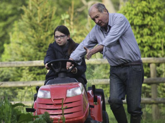 A man, who has chronic lymphocytic leukaemia, standing next to a girl on a lawnmower in a garden.