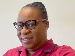 A middle aged Black woman in glasses and a pink shirt.