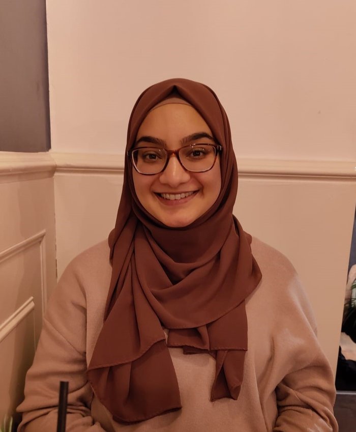 Nabeela, a young woman wearing glasses and a headscarf, smiling at the camera
