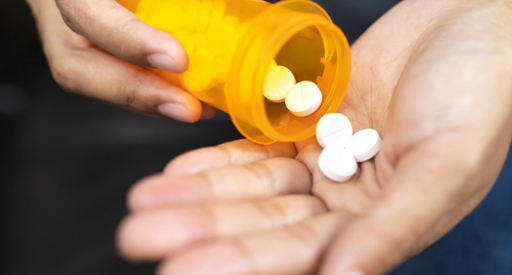 Close-up of pills being emptied from a plastic container into a hand.