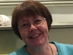 A headshot of a lady with short brown hair and glasses smiling.