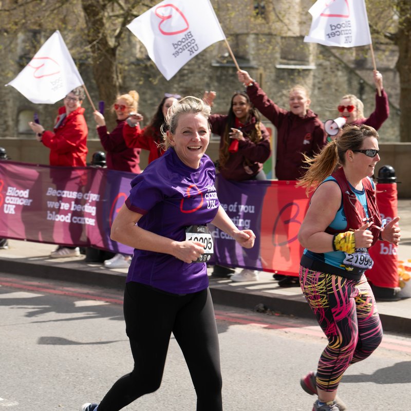 Blood Cancer UK female runner looking to camera with cheer point in the background