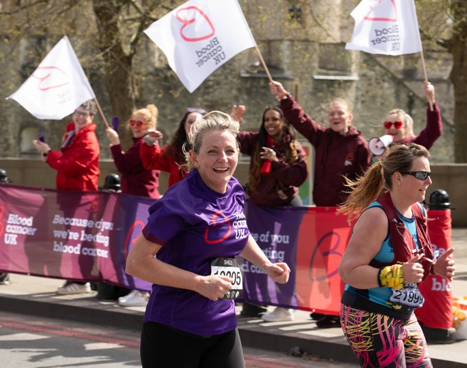 Blood Cancer UK female runner looking to camera with cheer point in the background