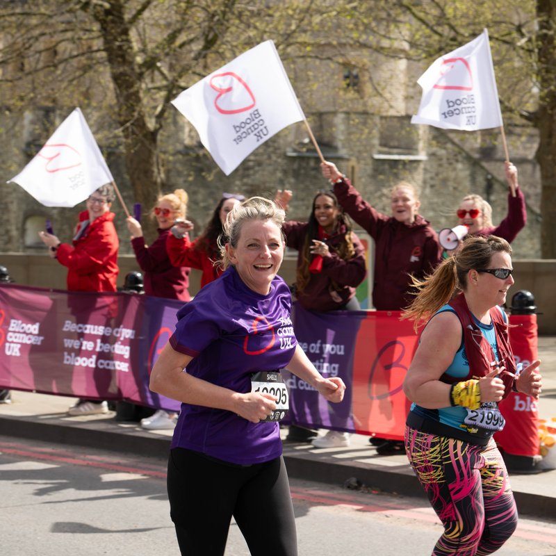 Blood Cancer UK female runner looking to camera with cheer point in the background