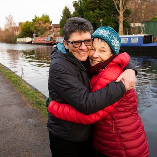 Two women hugging on a tow path, canal and boats in the background