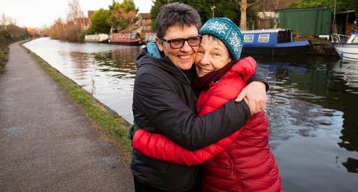 Two women hugging on a tow path, canal and boats in the background