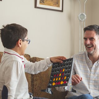Brett Grist, living with blood cancer, playing Connect 4 on a sofa with his son.