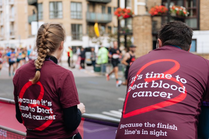 Two people wearing Blood Cancer UK t shirts, standing at a cheer point.