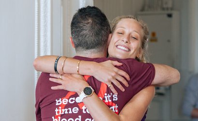 Two people hug and smile, wearing a Blood Cancer UK t-shirt.