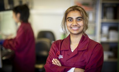A researcher smiles at the camera, wearing a burgundy Blood Cancer UK lab coat