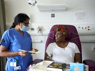 A healthcare professional and patient looking at each other. The patient is sitting in a chair having treatment administered.