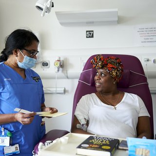 A healthcare professional and patient looking at each other. The patient is sitting in a chair having treatment administered.