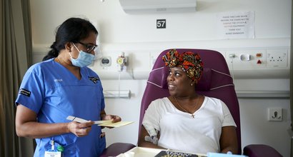 A healthcare professional and patient looking at each other. The patient is sitting in a chair having treatment administered.