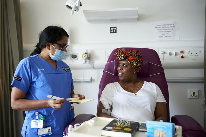 A healthcare professional and patient looking at each other. The patient is sitting in a chair having treatment administered.