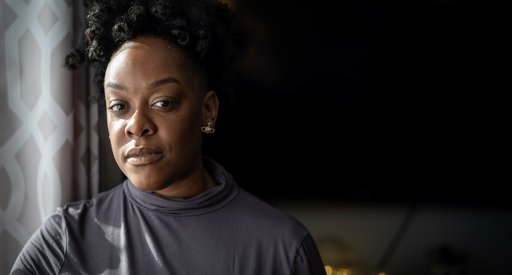 A close up of a black girl looking straight into the camera, light shining on her face with the background surrounded in shadows.