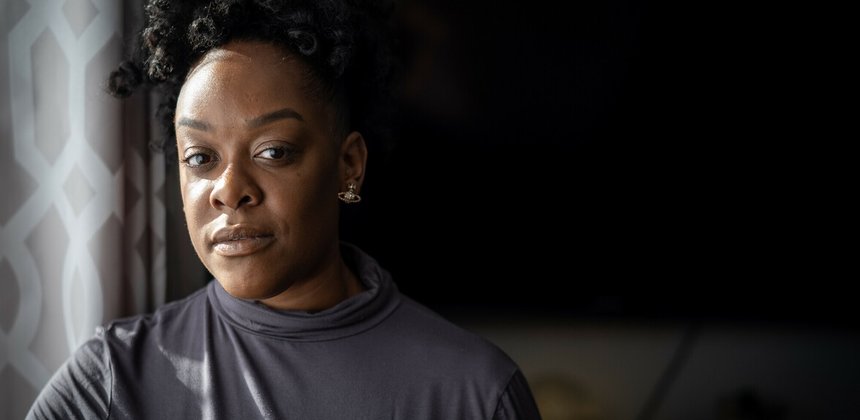 A close up of a black girl looking straight into the camera, light shining on her face with the background surrounded in shadows.