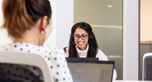 Woman smiling and speaking on the phone with headphones and laptop.