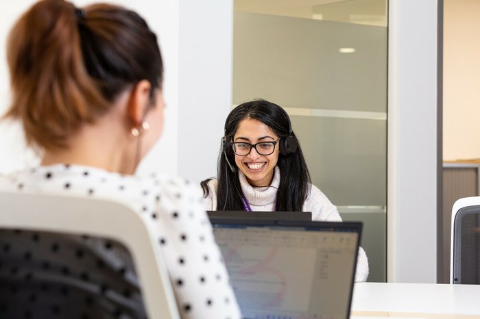 Woman smiling and speaking on the phone with headphones and laptop.