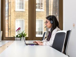 Woman talking on the phone with headphones and computer.