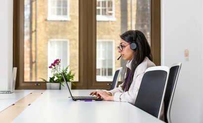 Woman talking on the phone with headphones and computer.