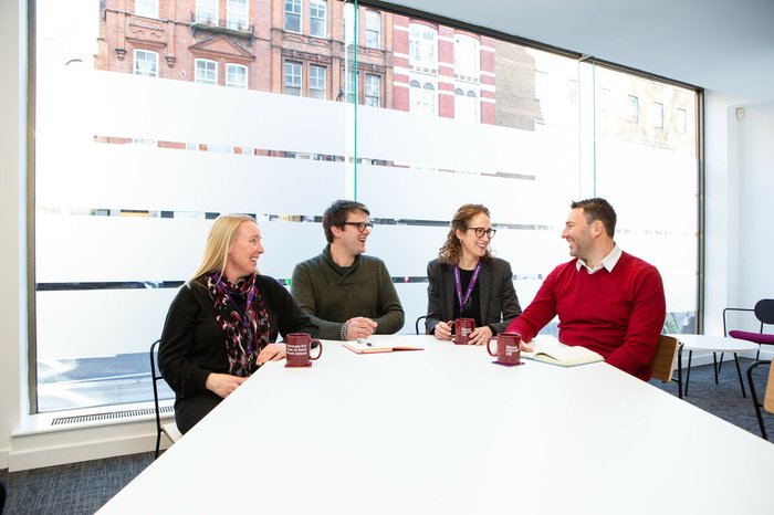 The executive team sitting in the Blood Cancer UK office, talking and smiling.