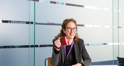 Blood Cancer UK's CEO, Helen Rowntree, holding a Blood Cancer UK coffee mug in the office and smiling.