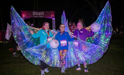 Three women wearing light-up fairy wings under the night sky at the Walk of Light event.