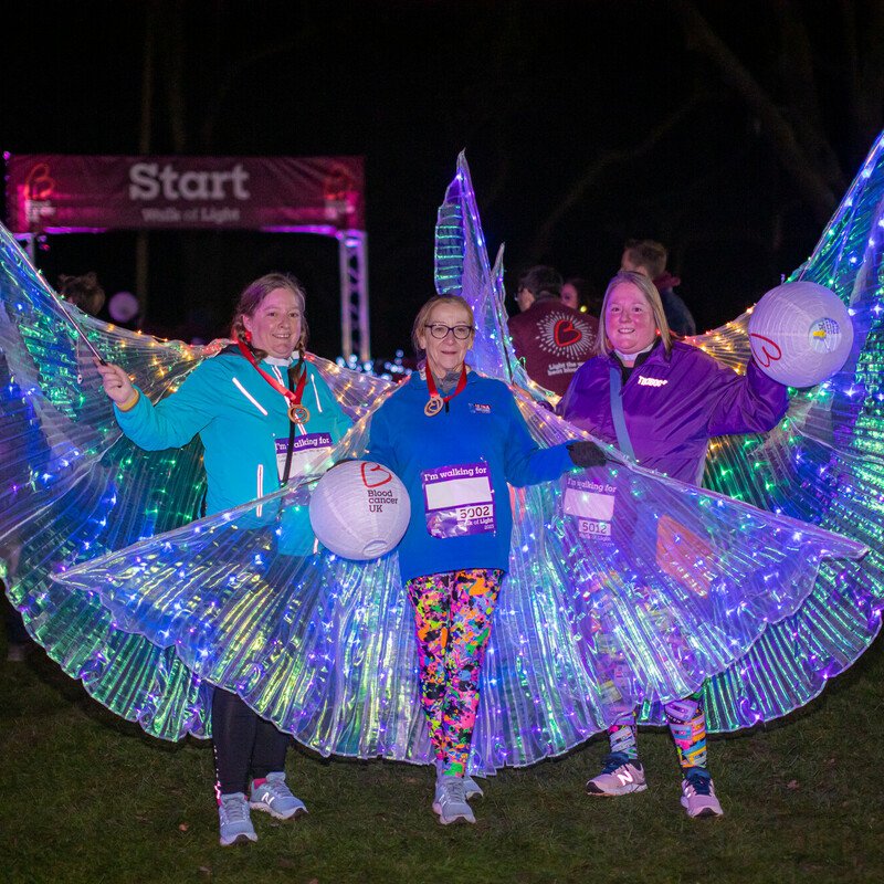 Three women wearing light-up fairy wings under the night sky at the Walk of Light event.