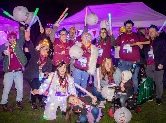 A group of people at the Walk of Light event, covered in fairy lights and decor as they stand under the night sky.