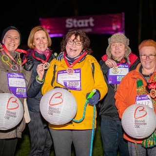Elizabeth and friends all smiling under the night sky, carrying their lanterns and showing off their medals after completing the Walk of Light.