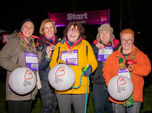 Elizabeth and friends all smiling under the night sky, carrying their lanterns and showing off their medals after completing the Walk of Light.