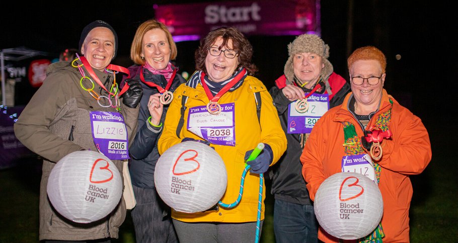 Elizabeth and friends all smiling under the night sky, carrying their lanterns and showing off their medals after completing the Walk of Light.