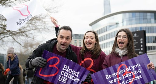 Blood Cancer UK staff members cheering and smiling at an event, holding flags and banners.