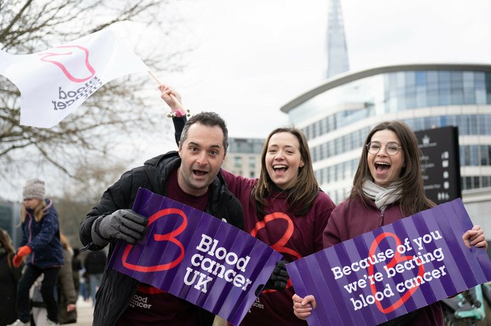 Blood Cancer UK staff members cheering and smiling at an event, holding flags and banners.