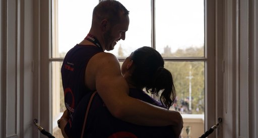 Man and woman hugging, standing by a window.