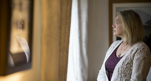 An older woman, at home, looking pensively out of the window.